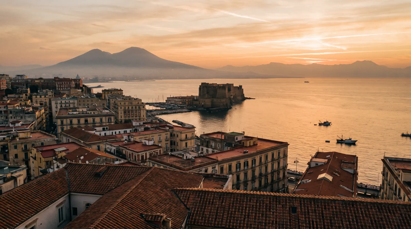 Vista panoramica del Golfo di Napoli al tramonto con il Vesuvio sullo sfondo e Castel dell'Ovo