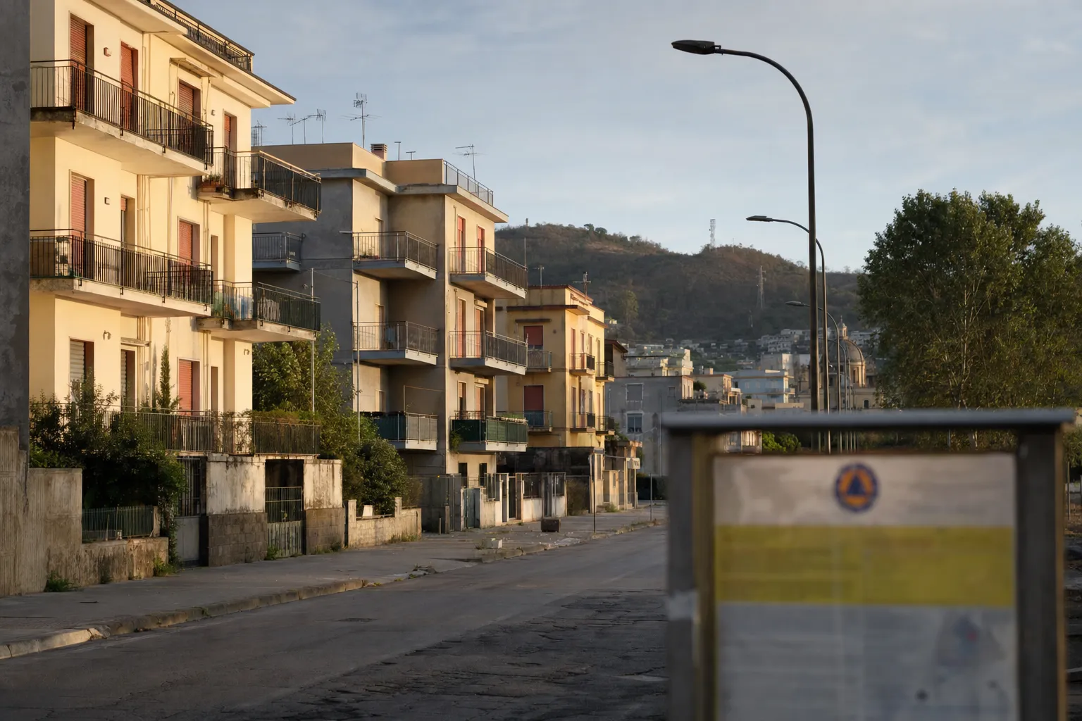 Strada residenziale a Pozzuoli con edifici sgomberati e cartello informativo della Protezione Civile